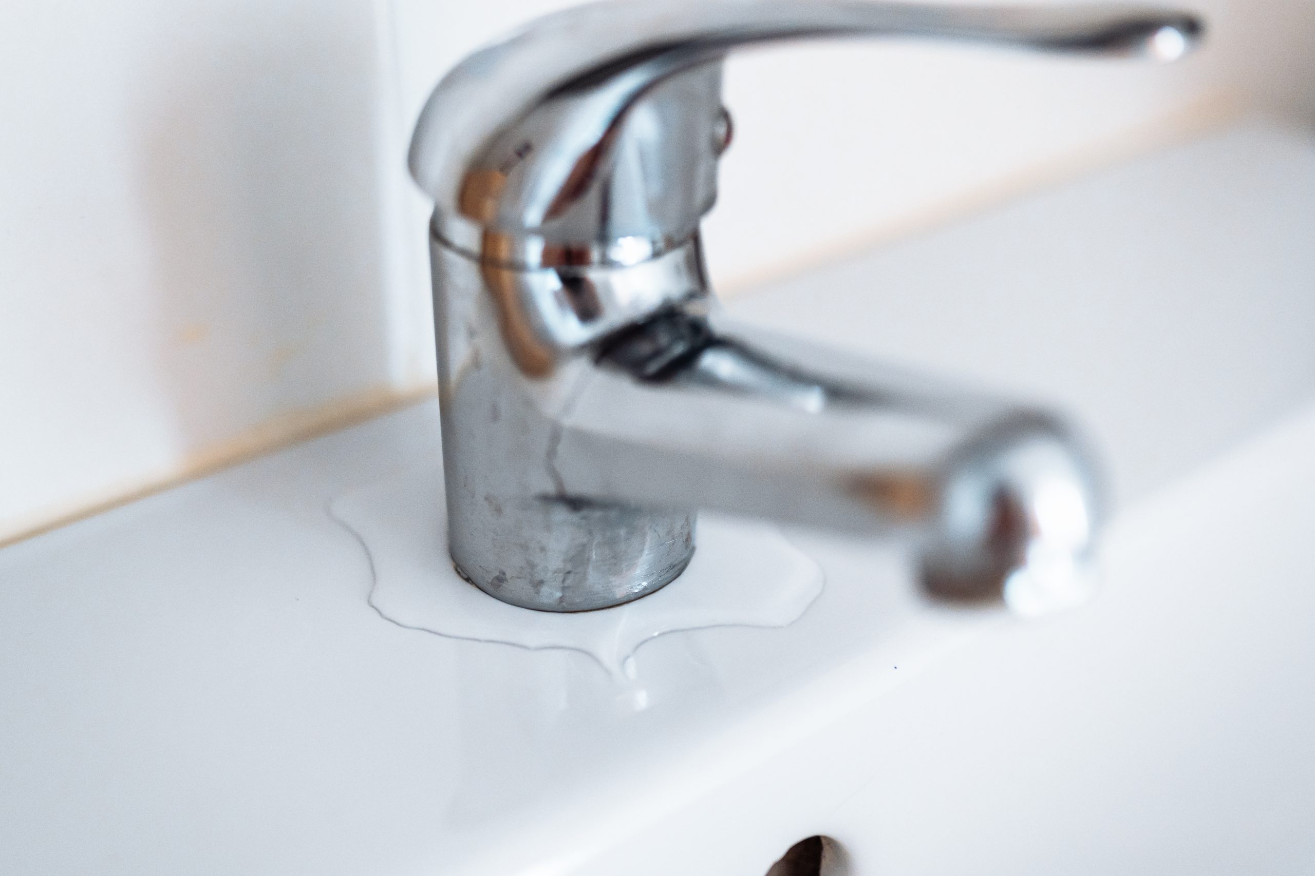 Close-up of a leaking bathroom tap with water pooling around the base, showing an early sign of a hidden water leak.